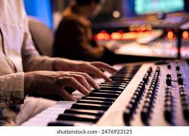 Artist performer recording his song on electronic keyboard piano, working with audio engineer in professional studio and producing new music. Singer composes on synthesizer. Close up.