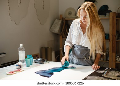 Artist pouring paint on paper making an art picture standing in front of a table in a home Studio