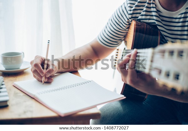 artist songwriter thinking and writing\
notes,lyrics in book at studio.man playing live acoustic\
guitar.concept for musician creative.composer in work\
process.people relaxing time with\
instrument