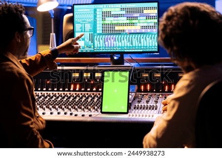 Artist and sound engineer working with greenscreen display on tablet, mixing and mastering tracks with audio console and digital software. Musicians team editing music, motorized faders.