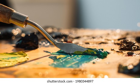 Artist work. Painting art. Professional craft. Spatula mixing blue yellow black oil or acrylic paint colors on old stained wooden palette.