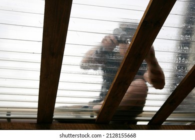 Artistic abstract view through roofing. Man worker working, using power tool to attach clear PVC roofing sheets on home terrace outdoors. Selective focus on wood beam. - Shutterstock ID 2128155668