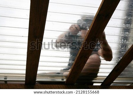 Artistic abstract view through roofing. Man worker working, using power tool to attach clear PVC roofing sheets on home terrace outdoors. Selective focus on wood beam.