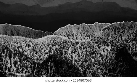 An artistic black and white aerial view shows large waves crashing against a sandy beach, creating interesting patterns on Sawarna Beach, Banten, Indonesia. - Powered by Shutterstock