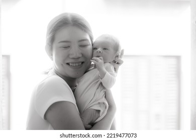 Artistic Black And White High Key Lifestyle Shot On Young And Happy Asian Chinese Woman Holding Adorable Newborn Baby Girl In Her Arms In Mother And Daughter Love Concept