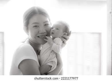 Artistic Black And White High Key Lifestyle Shot On Young And Happy Asian Chinese Woman Holding Adorable Newborn Baby Girl In Her Arms In Mother And Daughter Love Concept