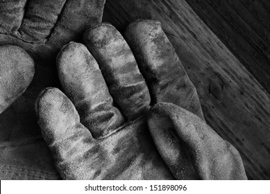 Artistic black and white image of well worn leather work gloves on wood background.  Low key still life with directional, natural lighting for effect.