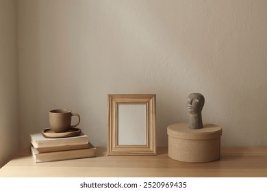 Artistic boho interior still life. Blank wooden photo frame mockup on table. Scandi interior decor. Cup of tea, coffee, old books. Boho busta sculpture, statue, round gift box. Beige wall background - Powered by Shutterstock