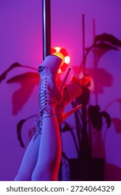 Художественный крупным планом полюс танцевальной платформы обувь и ноги на полюсе в студии с ярким розовым и фиолетовым светом.