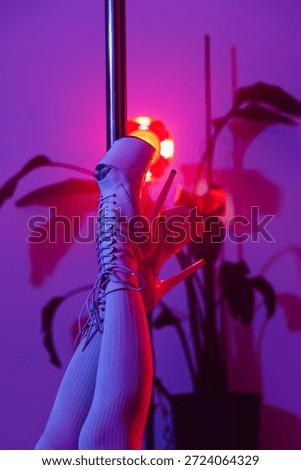 Artistic close-up of pole dance platform shoes and legs on  pole in studio with vibrant pink and purple light.