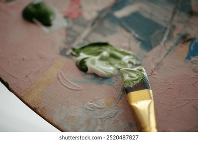 Artistic close-up showcasing paintbrush resting on paint palette with various paint blobs. Visible textures and colors emphasize process of creating an artwork - Powered by Shutterstock