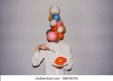 Artistic creative photography. Man wearing white shirt, delicate balloons and holding a sharp fork and a plate with balloon. - Shutterstock ID 588760745