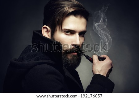 Artistic dark portrait of the young beautiful man. The young man smokes a tube. Close up