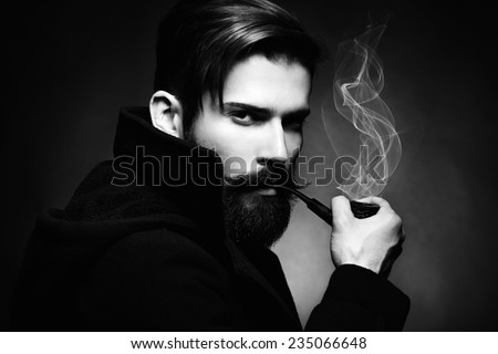 Artistic dark portrait of the young beautiful man. The young man smokes a tube. Close up. Black and white photo
