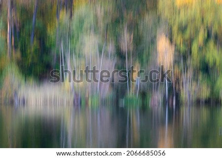 Artistic deliberate blur of mixed green and orange autumn trees by a lake