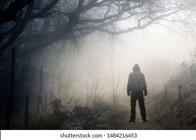 An artistic double exposure of a lone hooded figure on a path in the countryside on a spooky, foggy winters day.