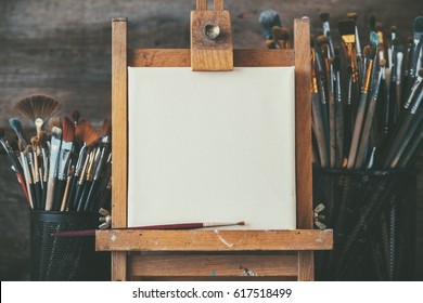 Artistic equipment in a artist studio: empty artist canvas on wooden easel and paint brushes Retro toned photo. - Shutterstock ID 617518499