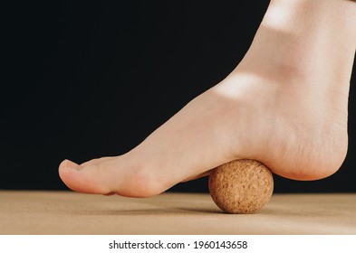 Artistic isolated close up foot on cork massage ball on cork yoga mat for plantar fascia massage and hydration on black background. Concept: self care practices at home
