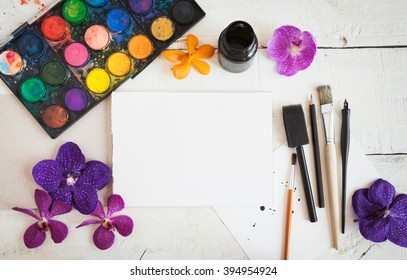 Artistic Mockup With Empty Notebook And Art Supplies Around Including Watercolor, Brushes And Calligraphy Pens. Blank Sketchbook On Wooden Desk.