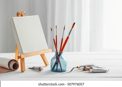 Artistic Paintbrushes, Canvas On Easel, Tubes Of Oil Paint, Palette Knife On White Wooden Desk.