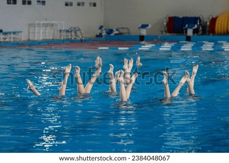 artistic performance in swimming pool, group of women doing synchrone moves in the water, legs synchronicity