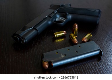 Artistic photo of a semi automatic 45 caliber handgun on a dark wood grain background with a loaded magazine and loose rounds of ammunition
