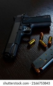 Artistic photo of a semi automatic 45 caliber handgun on a dark wood grain background with a loaded magazine and loose rounds of ammunition