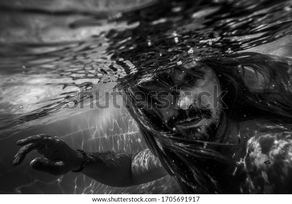 Artistic pic out of
focus underwater with long hair man swimming with bubble in water,
dark underwater atmosphere with nightmare human abyssal creature
like mermaid with
beard