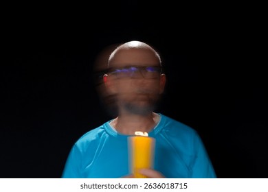 Artistic portrait of bearded bald man in blue shirt making motion blur effect with burning yellow candle. Light trail. Black background.