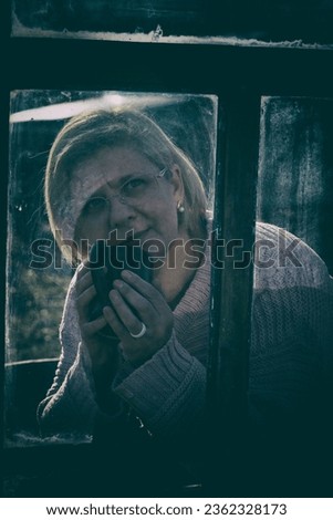 Artistic portrait of a woman looking out of the window to the street. He holds a mug with a drink in his hand. Portrait in the style of pictorialism. A woman is drinking hot drink from a mug. Close-u