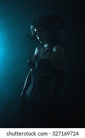 Artistic shot of a sensual gothic girl with horns on blue smoky background, Halloween theme 