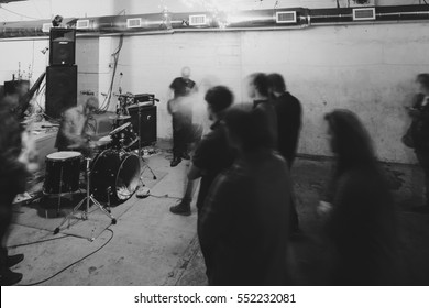 Artistic Shot Of Underground Concert With Drummer And Guitarists Playing For Concert Goers With Black And White Film Grain.