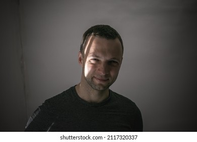 Artistic Studio Portrait Of A Young Adult Smiling Man Standing In The Shadow With A Sunlight Beam Over His Face