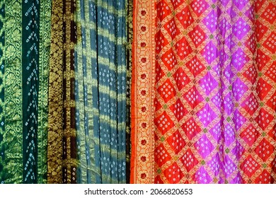Artistic variety shade tone colors ornaments patterns, closeup view of stacked saris or sarees in display of retail shop. 