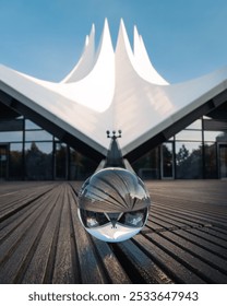 An artistic view of Tempodrom Berlin reflected in a glass sphere with wooden floor and blue sky.