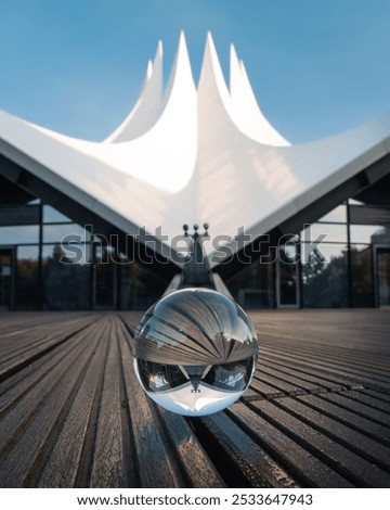 An artistic view of Tempodrom Berlin reflected in a glass sphere with wooden floor and blue sky.