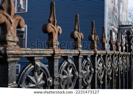 An artistic vintage rusty wrought iron fence with circular decorative symbols in between the rungs. There's a royal blue wooden building in the background. The ironwork has a star in the center.