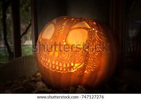 Artistically carved glowing jack-o'-lantern on tabletop display with leaves for Hallowe'en	