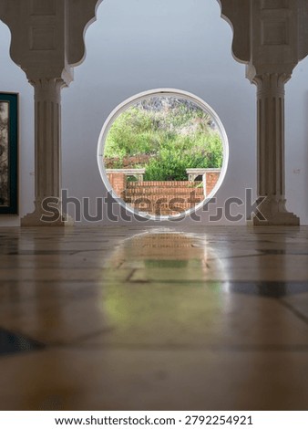 Artistically composed interior view emphasizing the glossy reflective quality of the patterned tiled floor which mirrors the soft glow emanating from a central circular window set within classical stone arches. The warm ambient lighting enhances the depth and luminosity of the space, drawing attention to the interplay of light, reflection, and the rhythmic geometry of the heritage architectural elements.