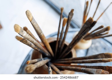 Artist's brush collection displayed in a wooden holder on a colorful table in a creative workspace - Powered by Shutterstock