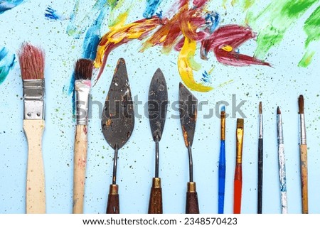 Artist's brushes, palette knives and paints on blue background
