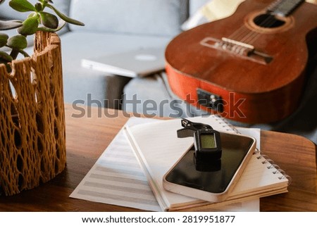 Artist's creative workspace featuring a classical guitar, clip on tuner, smartphone, notebook, and sheet music, representing the musical process of composition, learning, and productivity at home