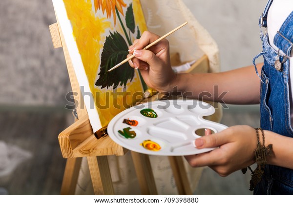 Artist\'s hand with brush and palette painting a picture\
Sunflower 