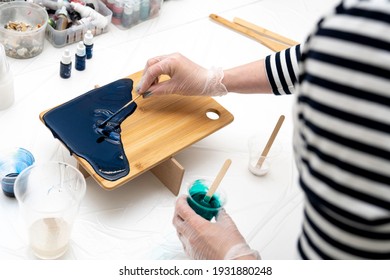 Artist's Hand Spreads Epoxy With A Spatula Over A Serving Wooden Board. DIY Craft For The Interior