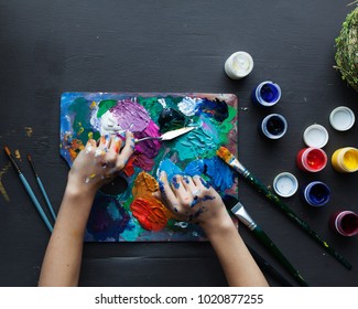 The artist's hands, paint palette brushes, different colors. The girl is drawing. The artist's tools for real art and inspiration. Dark light. Top View. - Powered by Shutterstock