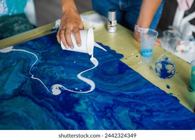 Artist's hands pouring white paint on blue swirl acrylic pour art - Powered by Shutterstock - Get 15% off with code: PIKWIZARD15