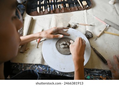 An artist's hands shape clay on a pottery wheel, surrounded by sculpting tools in a creative studio, a hands-on process of pottery making, craftsmanship and artistic expression.. - Powered by Shutterstock