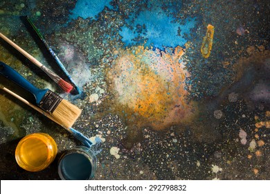 The artist's palette. Spray droplets and smears on a dark background. Nearby are open cans of paint and brushes.