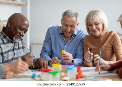 Art-therapy For Seniors Concept. Positive Multiracial Group Of Elderly People Enjoying Painting With Brush, Sitting Around Table, Having Good Time Together At Retirement Home, Closeup Photo