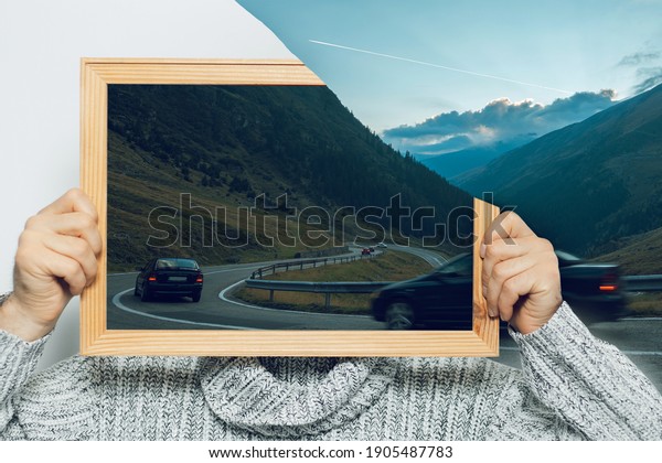 Artwork collage concept. Man holding a\
picture in frame on face. Landscape of mountains at sunset; cars\
driving on serpentines.